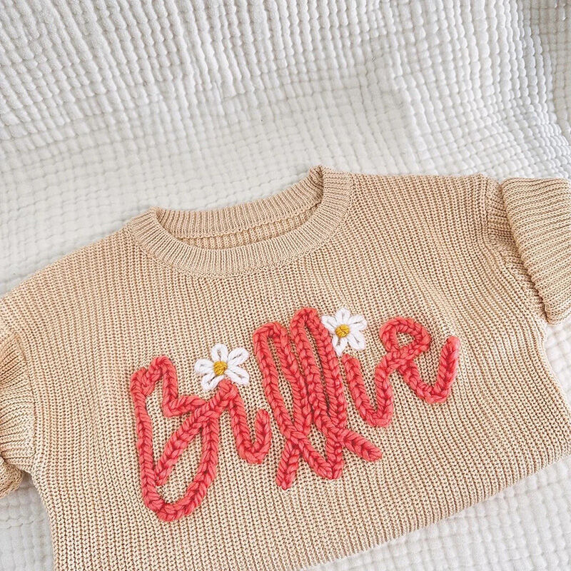 Suéter hecho a mano personalizado con nombre con flores blancas y texto rosa para niños