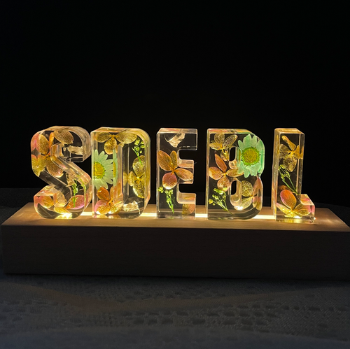 Lampe à lettres personnalisée en résine avec des pétales verts et des fleurs séchées.